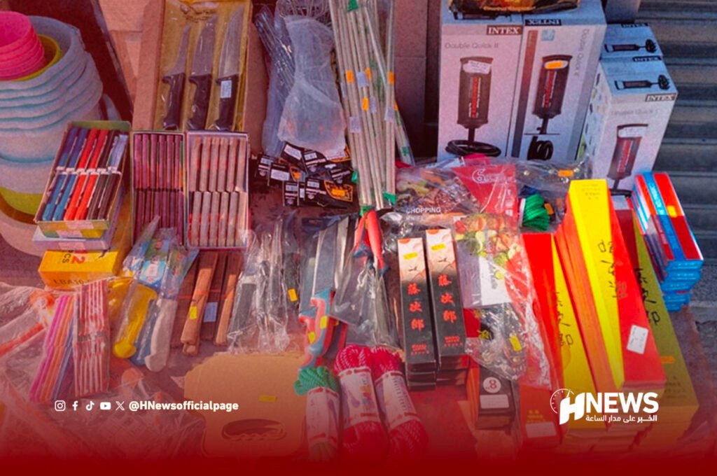 Colorful street market stall with knives, chopsticks, kitchenware, and assorted packaged items arranged on tables; HNews logo bottom right.