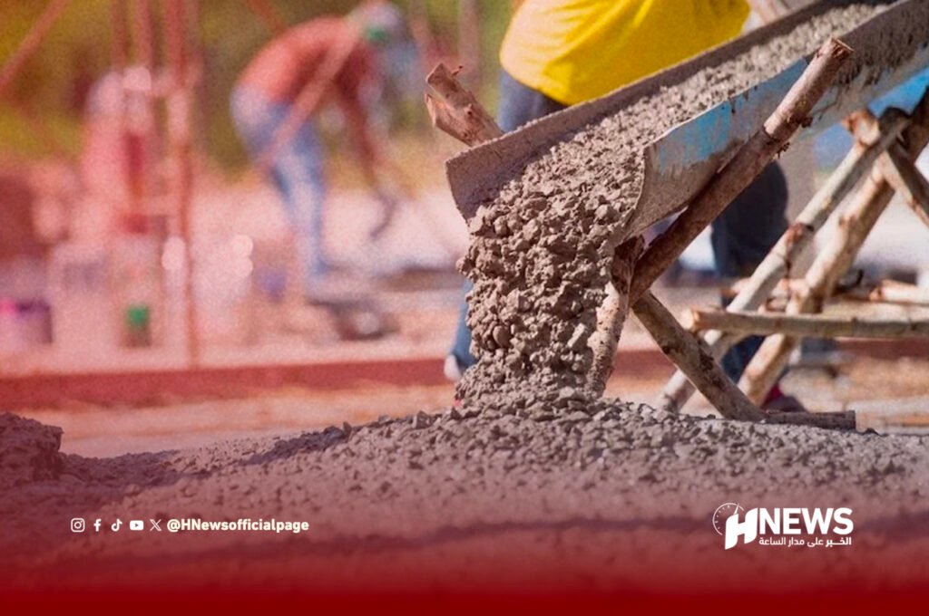 Close-up of wet concrete being poured onto a foundation, with construction workers and scaffolding in the blurred background.