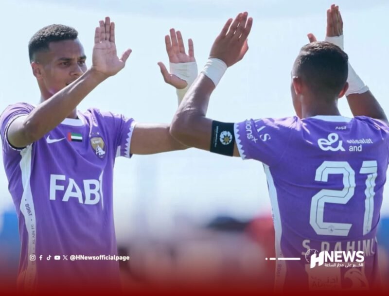Two soccer players in purple jerseys high-fiving on the field, one facing the camera and the other showing the number 21 on his back.