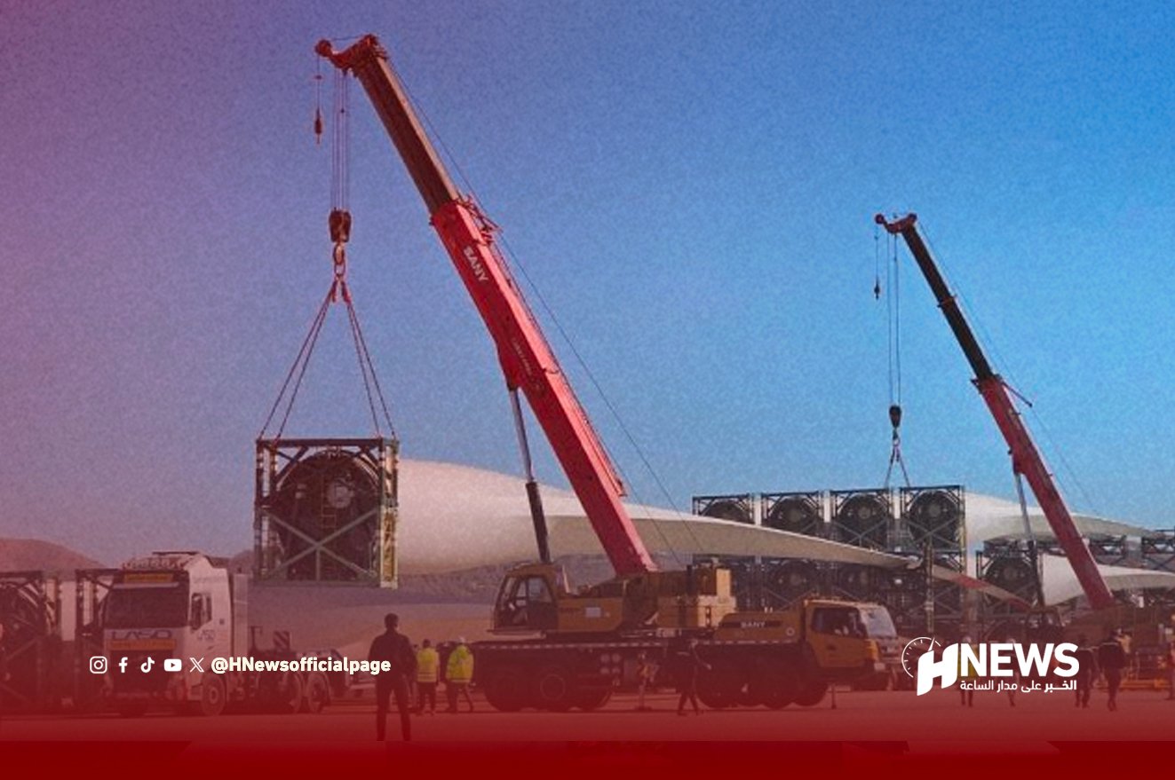 Crane trucks hoist large turbine components at a desert construction site with workers nearby and an HNews banner in the foreground.