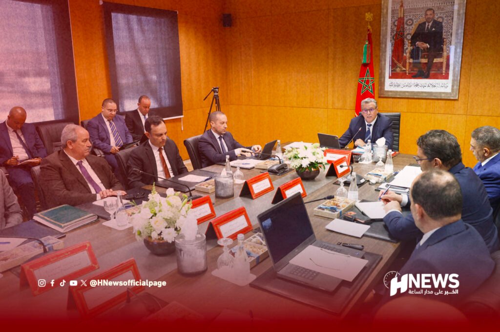 Group of officials in a boardroom around a long table, Moroccan flag and portrait in the background on wood-paneled walls.