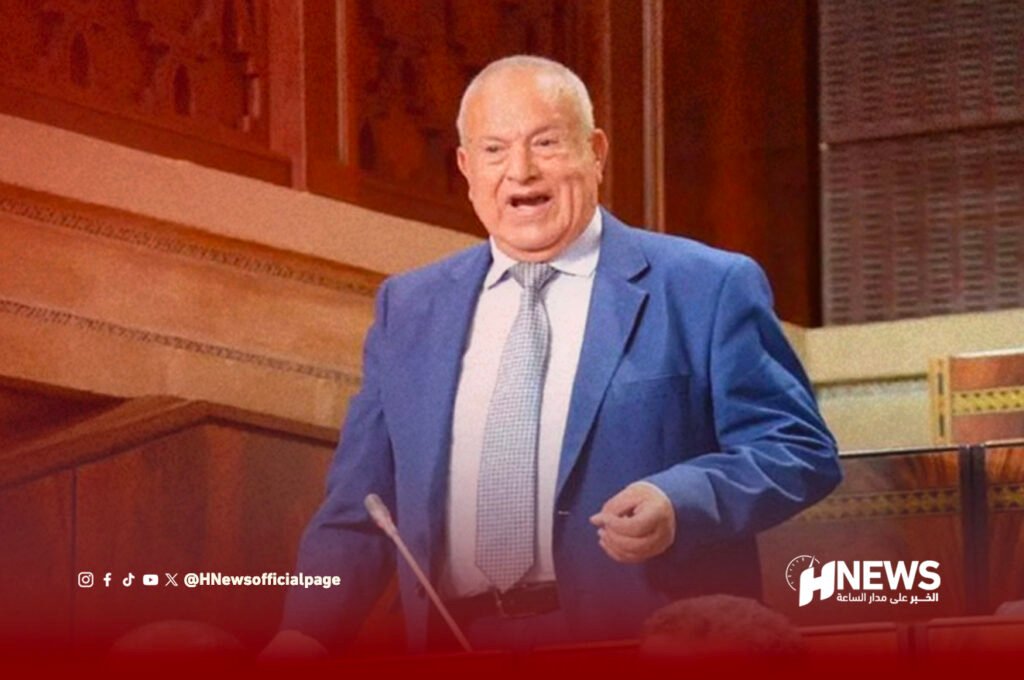 محمد أبركان | H-NEWS آش نيوز Elderly man in a blue suit speaks at a lectern in a formal chamber, with a red overlay and HNews watermark nearby.
