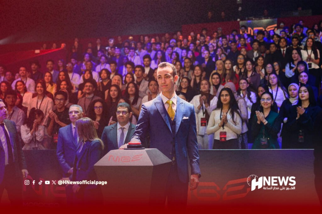 مولاي الحسن معرض الألعاب | H-NEWS آش نيوز Man in a blue suit presses a red button on a podium in front of a large applauding audience at a formal event, with HNEWS branding visible in the foreground.
