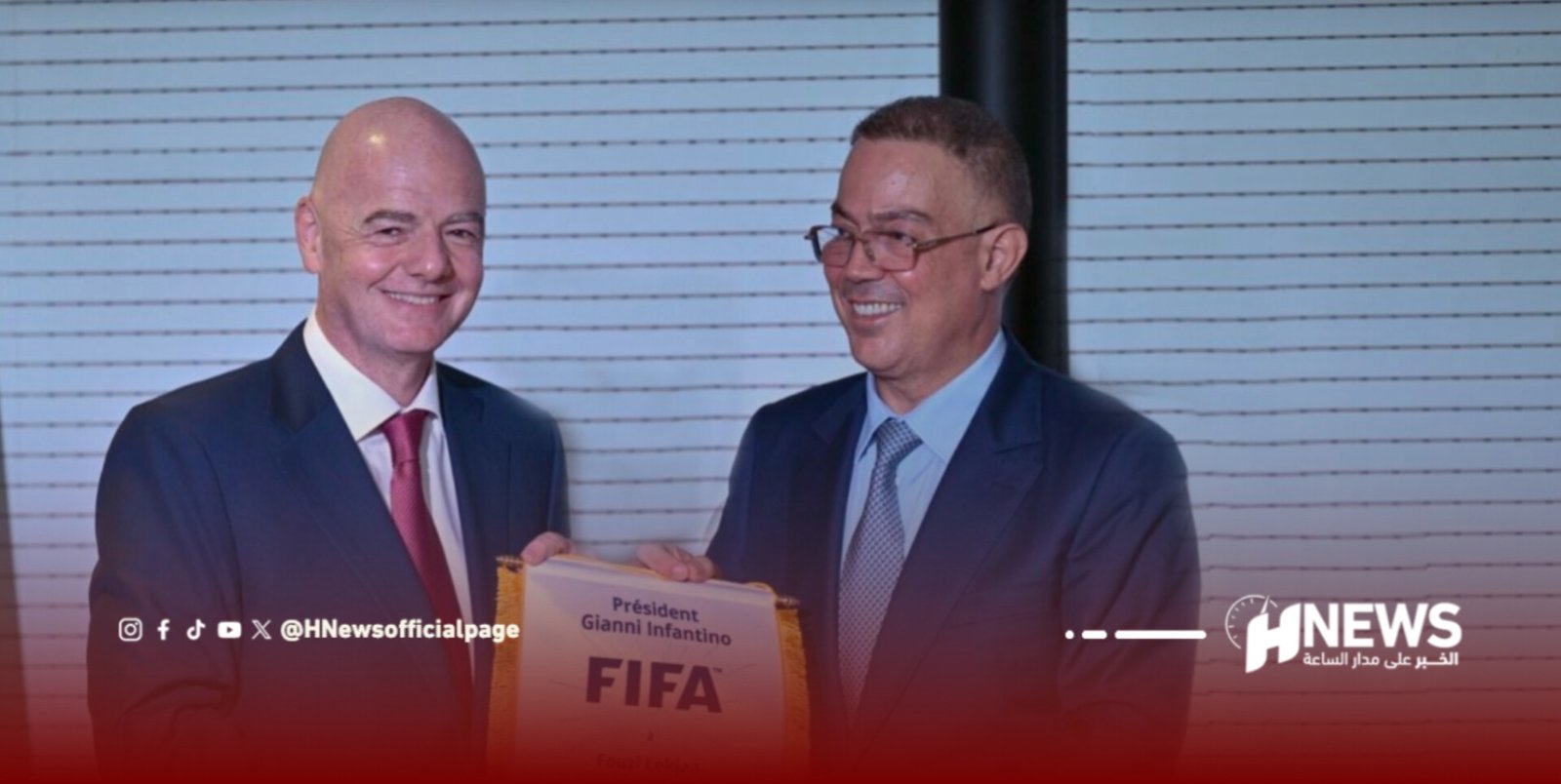 Two men in dark suits smiling and presenting a FIFA certificate, with the plaque text including 'FIFA' and 'Président Gianni Infantino' visible in the foreground.
