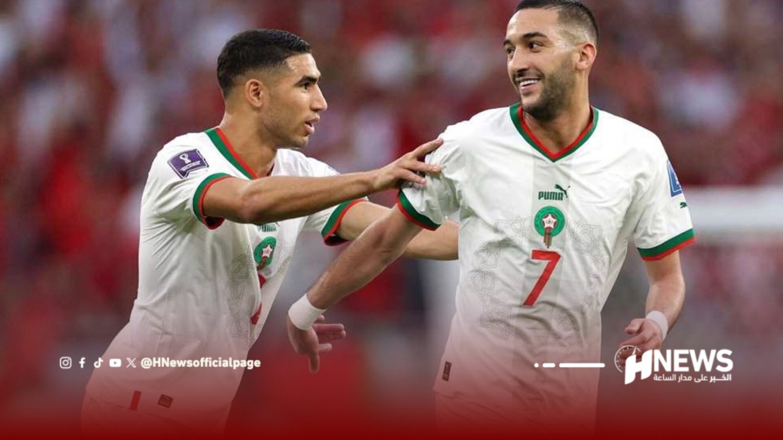 Two Algeria national team players celebrate on the soccer field, one reaching toward the other as they run together in white jerseys with green and red trim.