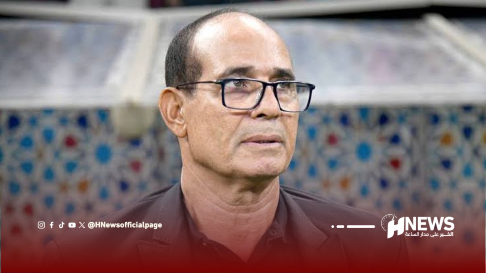 Man with glasses in a brown shirt, looking to the right, in a TV studio with a tiled backdrop and HNews watermark.