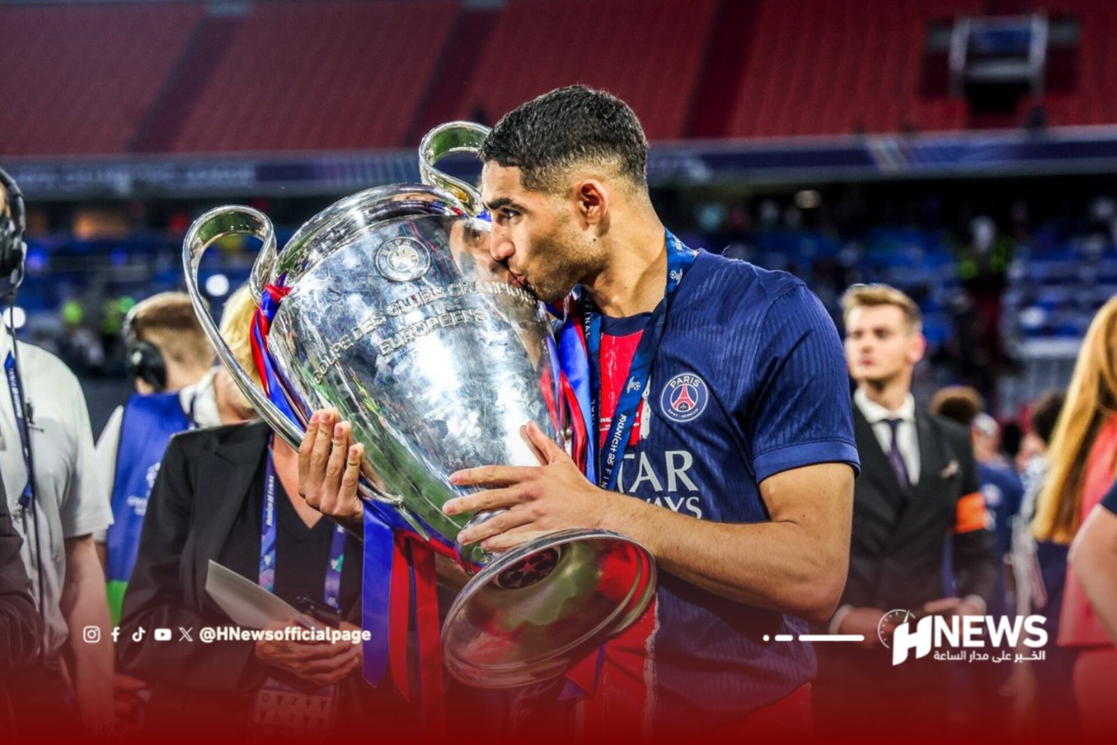 PSG footballer in a blue jersey kisses a large silver trophy during celebrations.