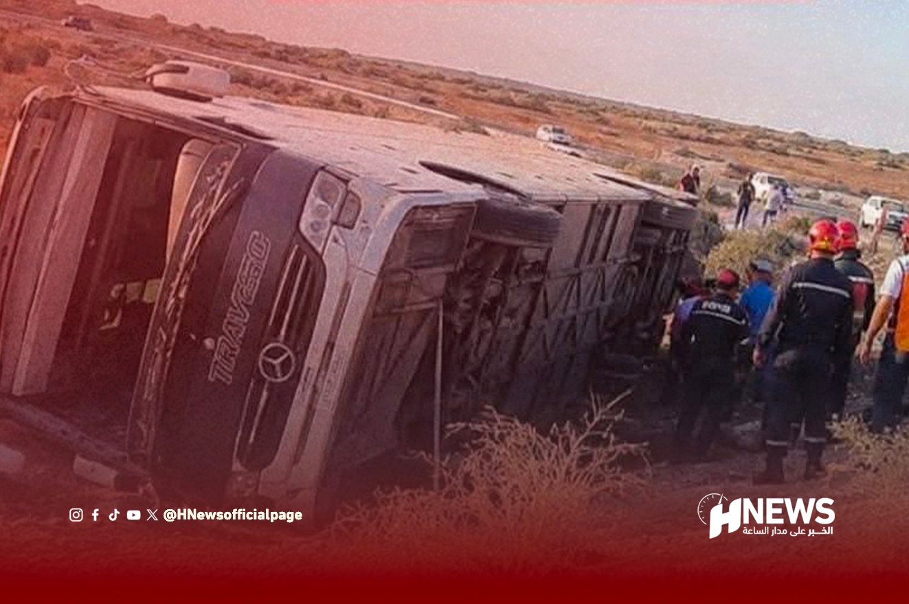 Overturned bus on its side after a crash, with emergency responders and bystanders at the scene on a rural road