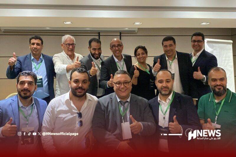 Group of twelve professionals at a conference posing for a thumbs-up photo, with HNews branding at the bottom right.
