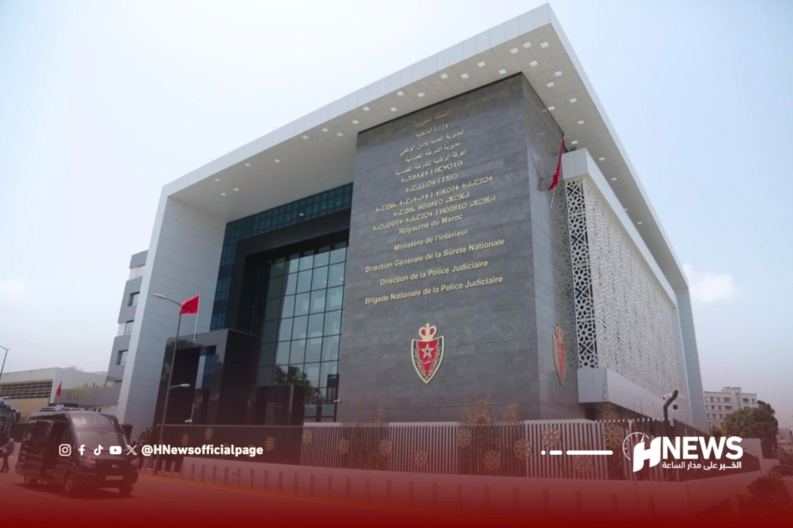 Front view of a modern Moroccan government building with a large stone plaque bearing gold Arabic inscriptions, crests, and red flags on the facade.