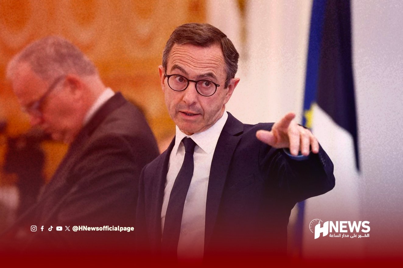 Man in a dark suit and glasses points outward at a press conference, with a blurred background and the HNEWS watermark visible at the bottom right.