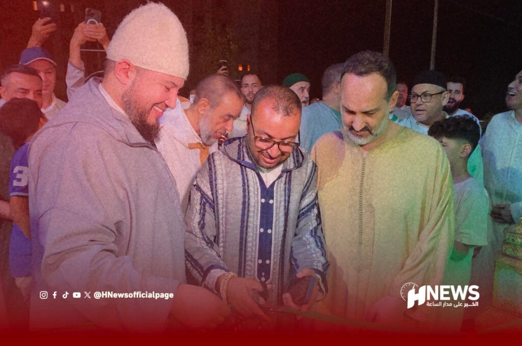 افتتاح الزاوية القادرية البودشيشية | H-NEWS آش نيوز Three men cut a red ribbon at a night-time ceremony, smiling, with a crowd behind them and HNEWS logo in the corner.
