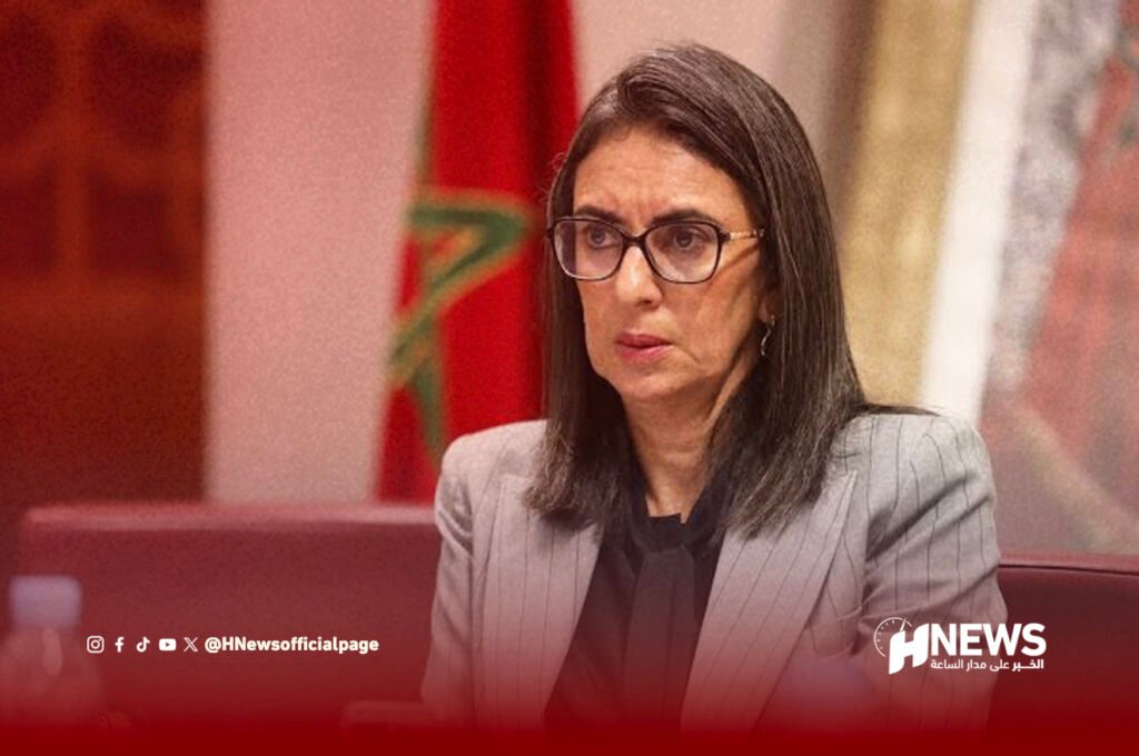 نادية فتاح العلوي | H-NEWS آش نيوز Woman in a gray pinstripe suit and glasses speaks at a press briefing; HNEWS watermark bottom right.