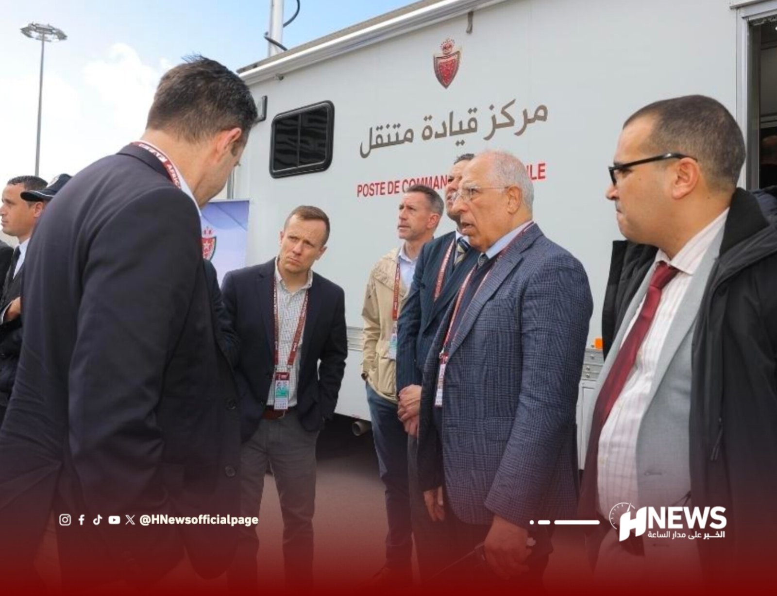 Group of suited men standing outside a mobile command center vehicle with Arabic lettering on its side.