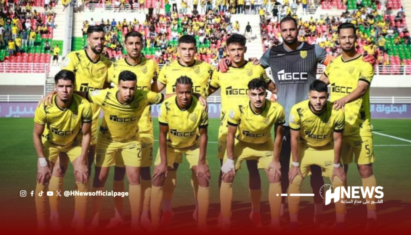 Soccer team in yellow kits posing for a group photo on the field with fans in the stands behind them.