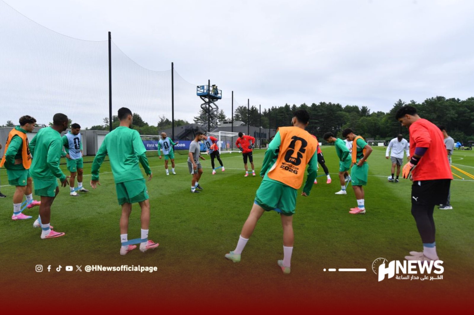Group of football players in green training kits warming up on a practice field, some wearing orange bibs.