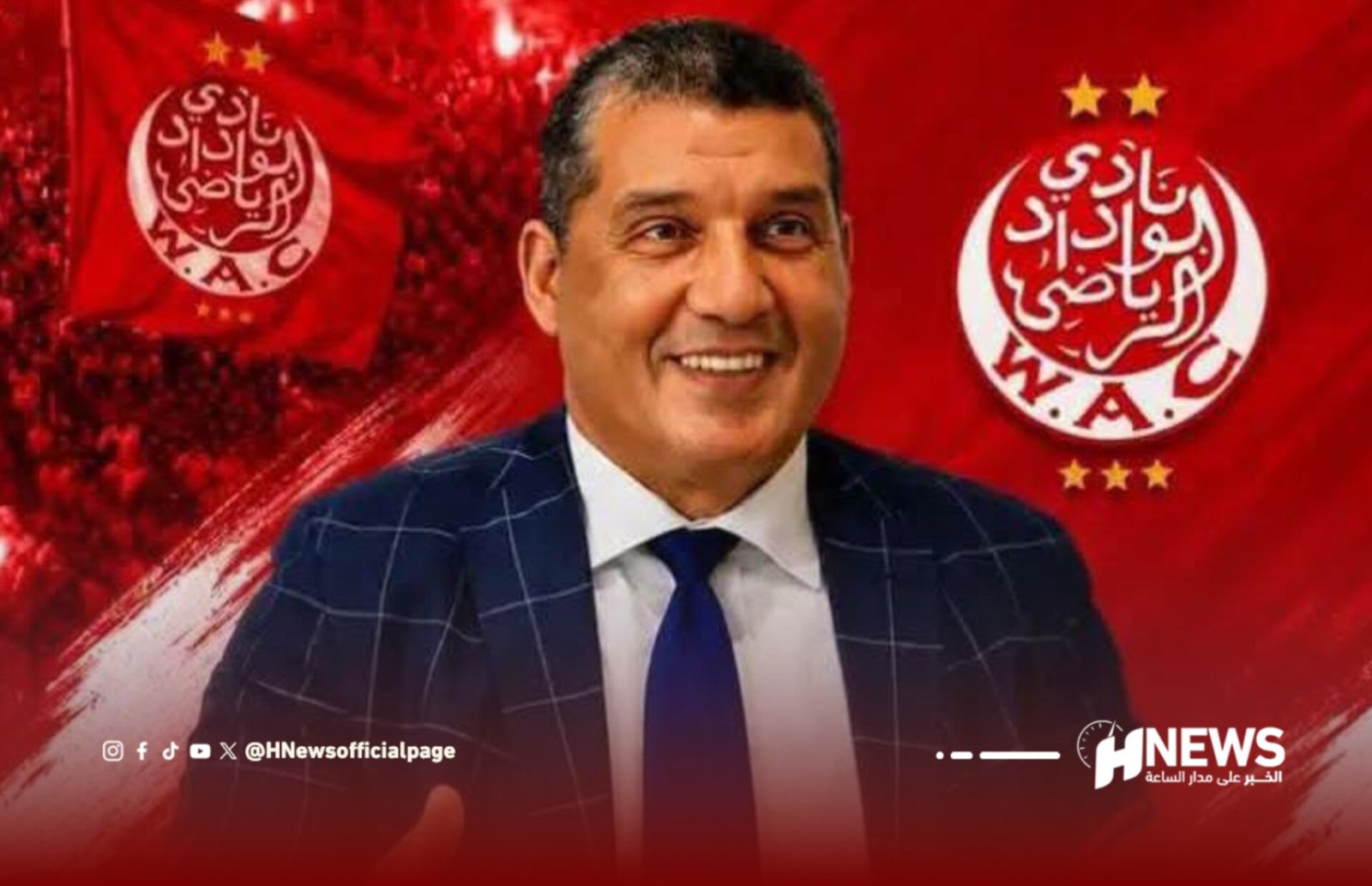 Smiling man in a dark blue checkered suit and blue tie stands in front of a red campaign backdrop with circular Arabic logos and star symbols behind him.