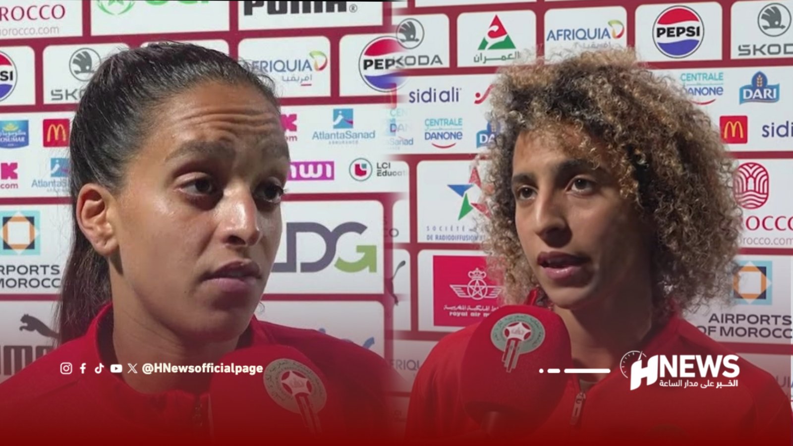 Two women in red sports outfits being interviewed, microphones in view, with a sponsor-filled backdrop behind them.