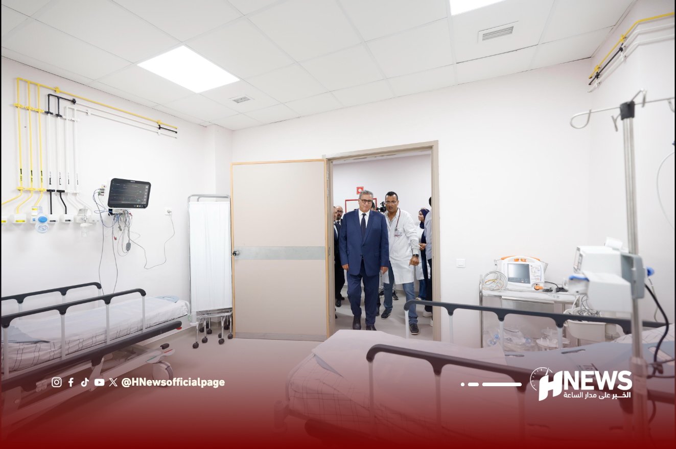أخنوش مستشفى 3 | H-NEWS آش نيوز Hospital ICU room with two empty beds and monitoring equipment; a suited man and medical staff enter through an open doorway from a group.