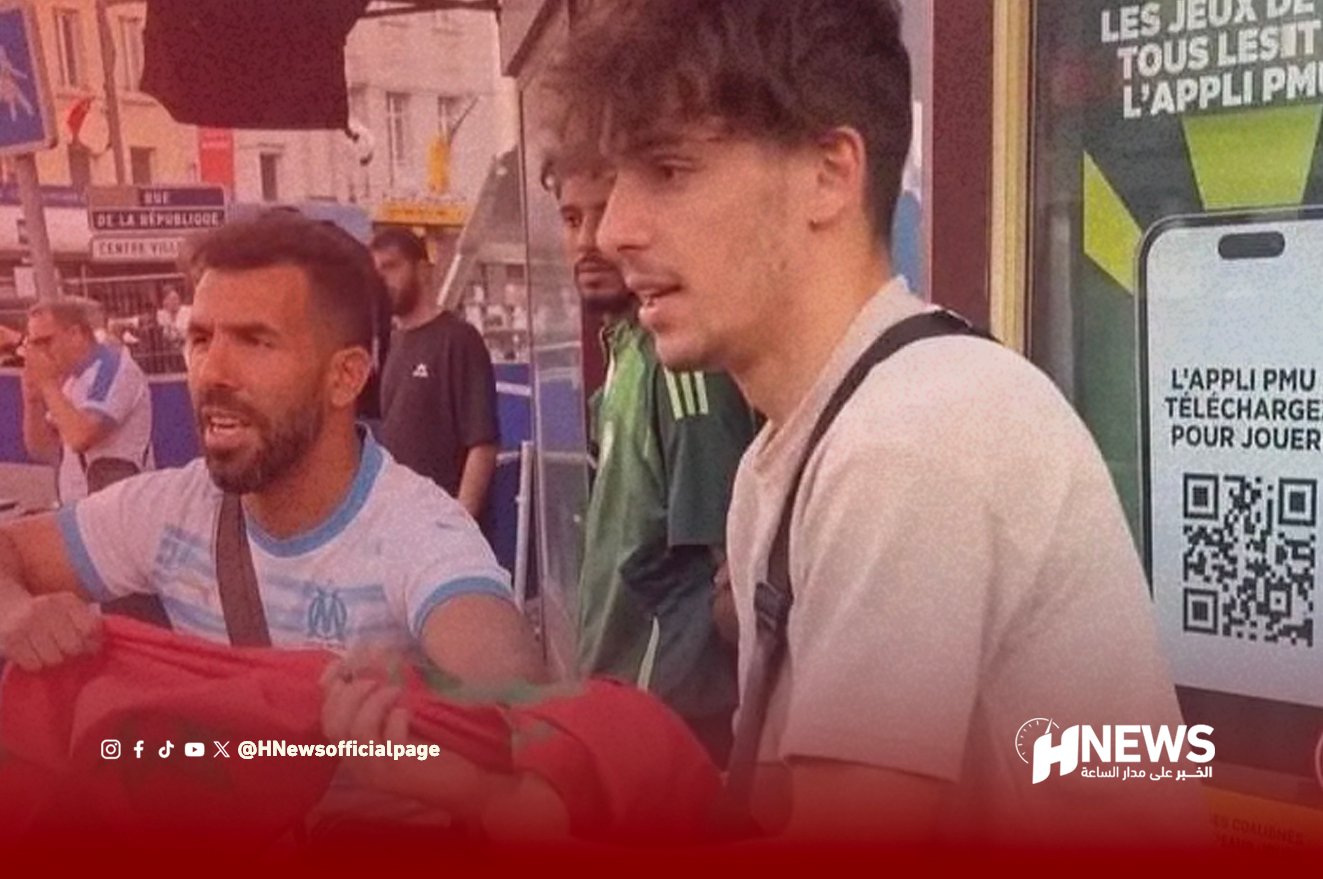 Two men on a city street talking, one holding a red flag and the other wearing a shoulder bag, with a news logo visible in the corner.
