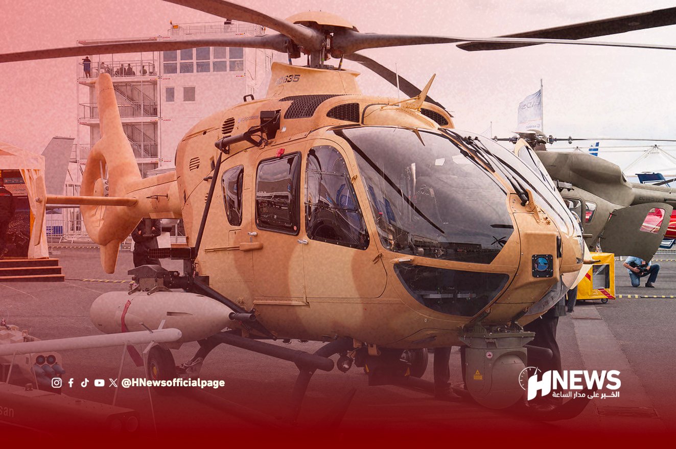 Tan helicopter on display at an air show, with people and a building in the background and the HNEWS logo bottom right.