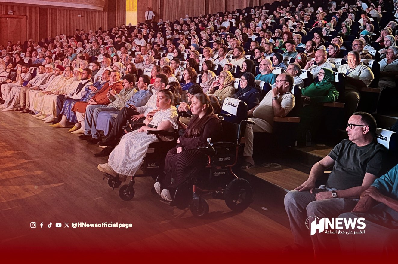 ياض النور 2 | H-NEWS آش نيوز Wide shot of a crowded theater audience, with a woman in a motorized wheelchair in the front row and a red fade at the bottom with the HNews logo shift to the right corner.
