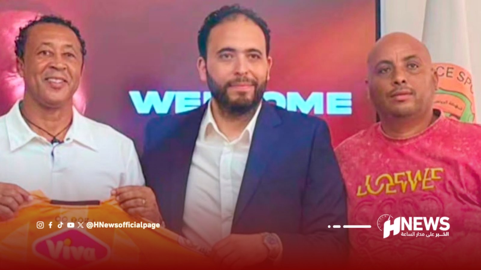 Three men sit together in front of a red backdrop with a partially visible 'WELCOME' sign behind them, smiling for the photo (press/news setting).