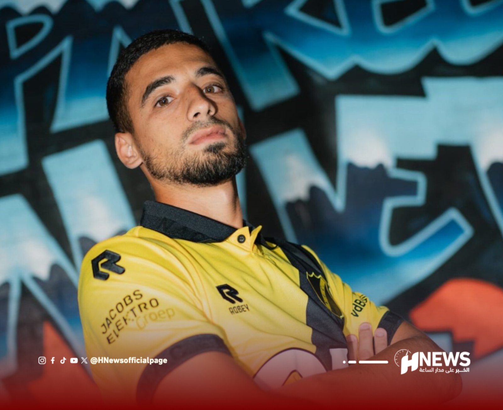 Portrait of a man in a yellow sports jersey posed against a graffiti-covered wall, looking at the camera.
