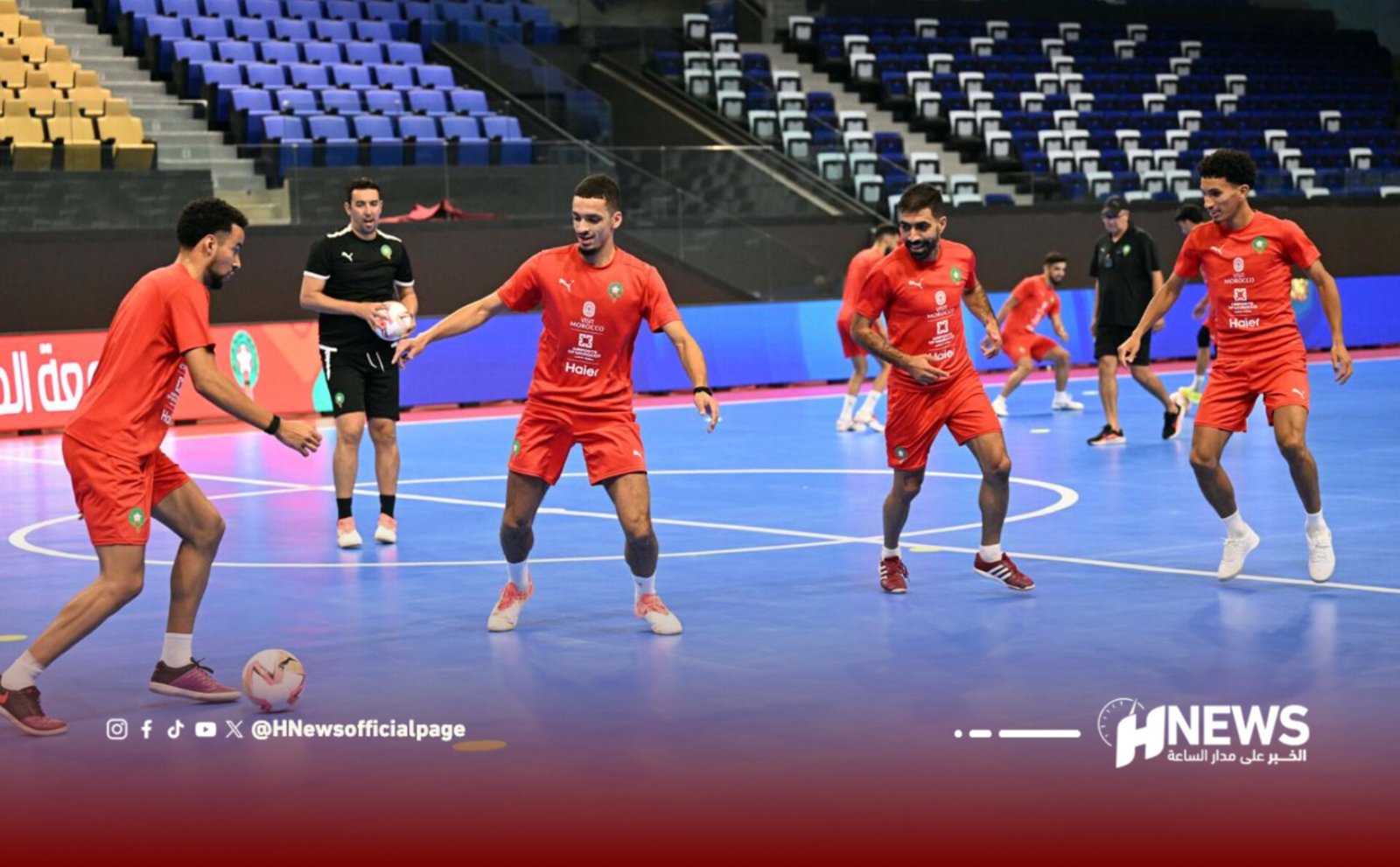 Futsal players in red jerseys pass the ball on a blue indoor court with empty spectator stands in the background; H News watermark bottom right.