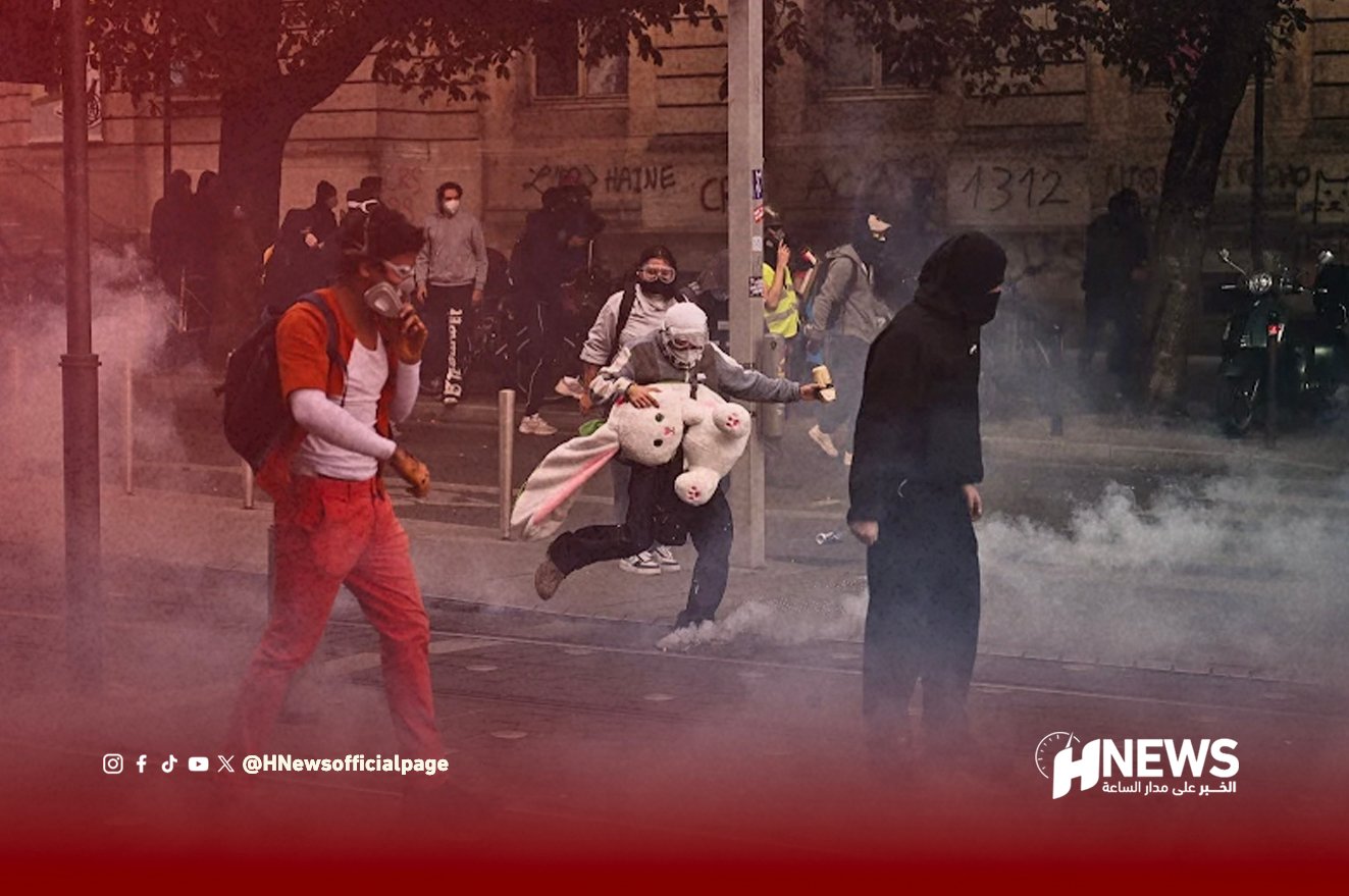 Protest scene with smoke on a street; masked demonstrators run, including a person in orange with a backpack and a large white stuffed bunny nearby.